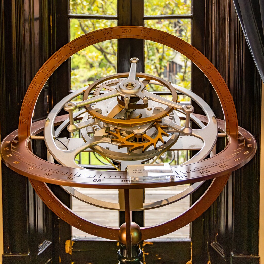 A photo of an antique brass armillary sphere displayed in front of a sunlit window
