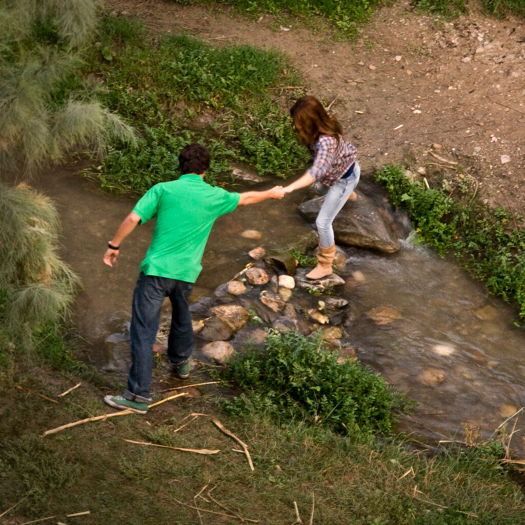 A man helping a woman across a stream