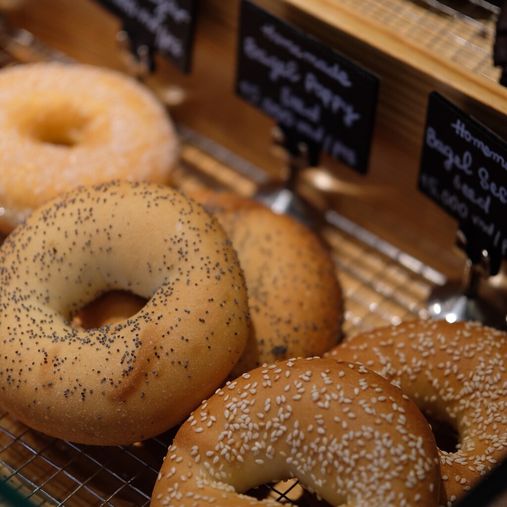 Several fresh sesame and poppy seed bagels in a bakery display.
