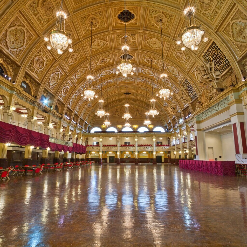 A photo of an ornate ballroom with a large polished dance floor and chandeliers.