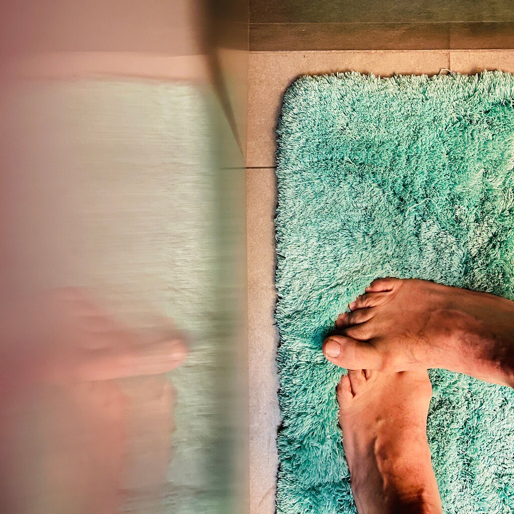 A photo of feet standing on a soft green bath mat beside a bathroom fixture