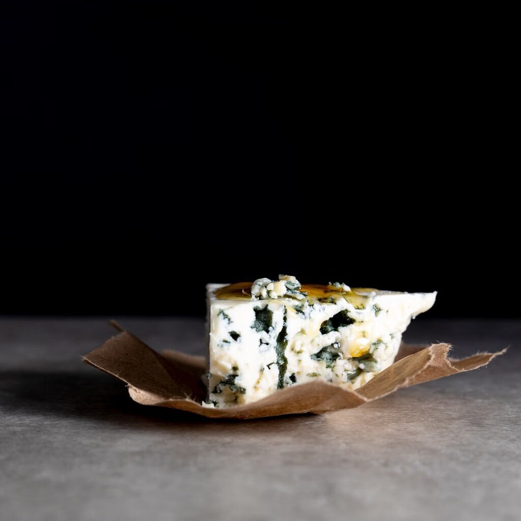 A photo of a wedge of blue cheese on brown paper.