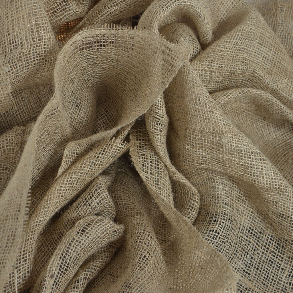 A photo of loosely woven burlap fabric draped in folds against a white brick wall