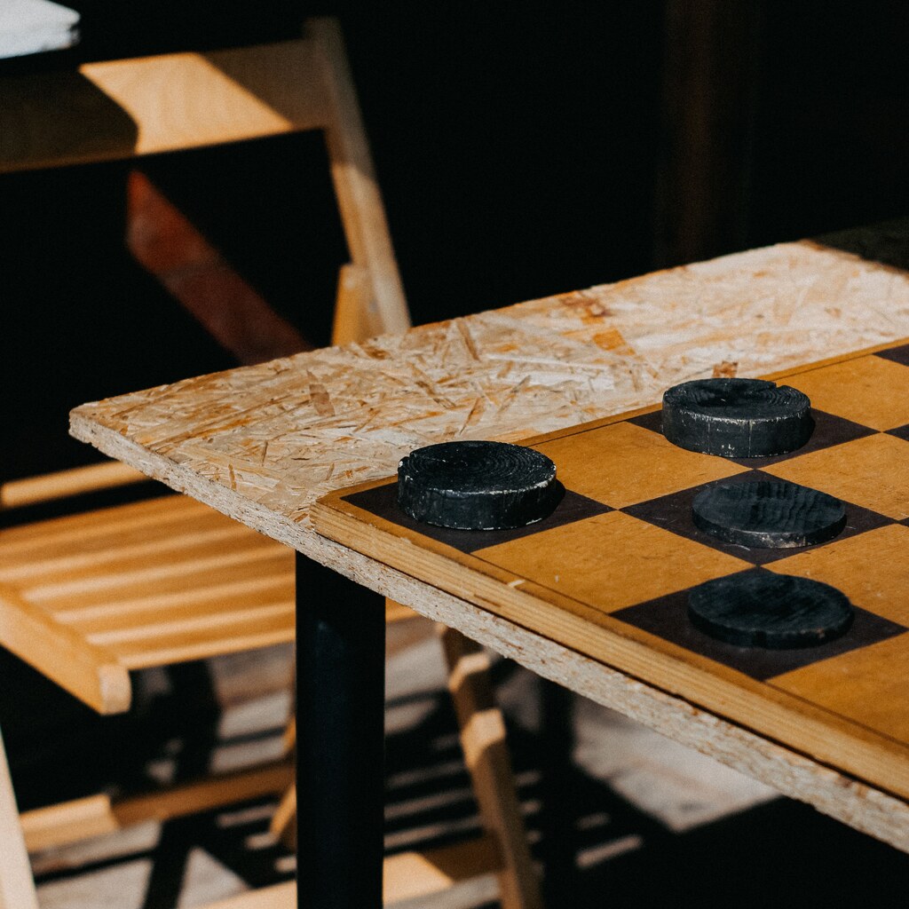 A photo of a wooden checkers board with black pieces on a rustic table