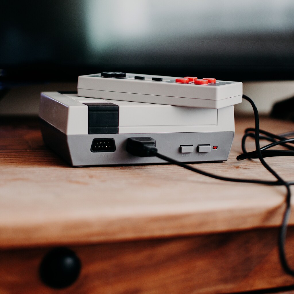 A photo of a vintage video game console with a controller on a wooden desk