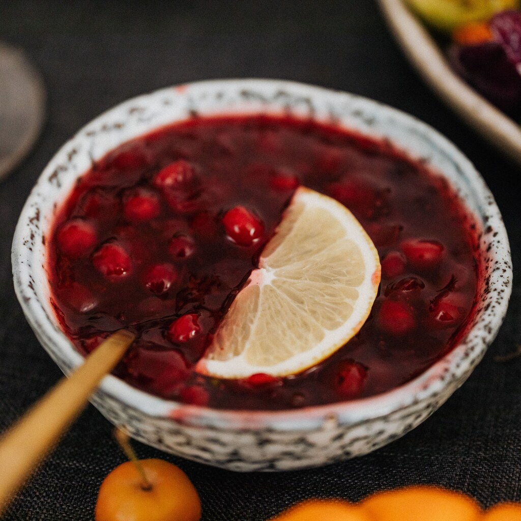 A photo of cranberry sauce with whole cranberries in a ceramic bowl, garnished with a lemon slice