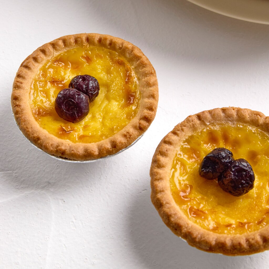 A photo of two golden custard tarts topped with raisins