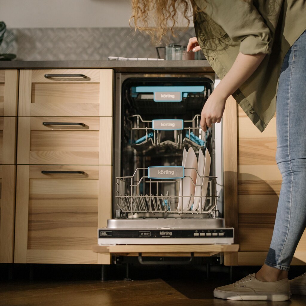 An open dishwasher with racks of plates as a woman loads it.