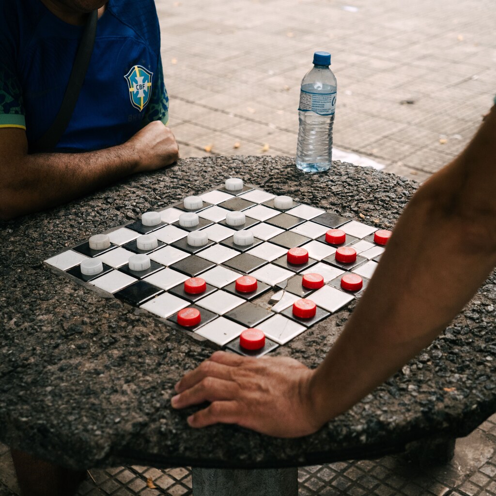 A photo of two people playing checkers on a stone table outdoors