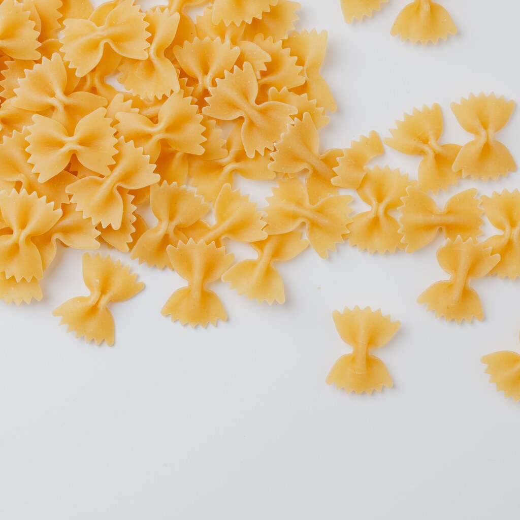 A photo of uncooked bowtie-shaped farfalle pasta scattered on a white surface