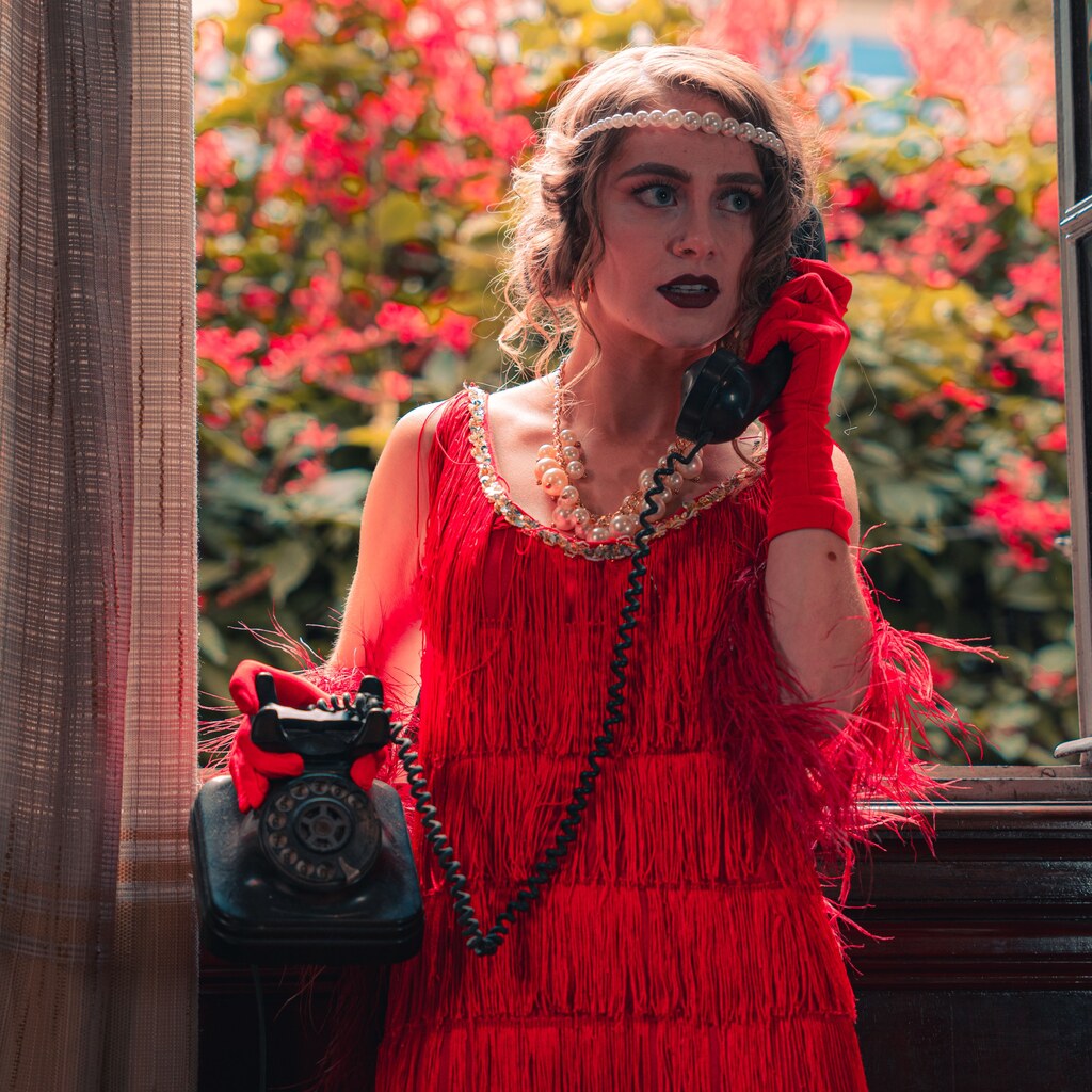 A photo of a woman in a red 1920s flapper dress holding a vintage telephone