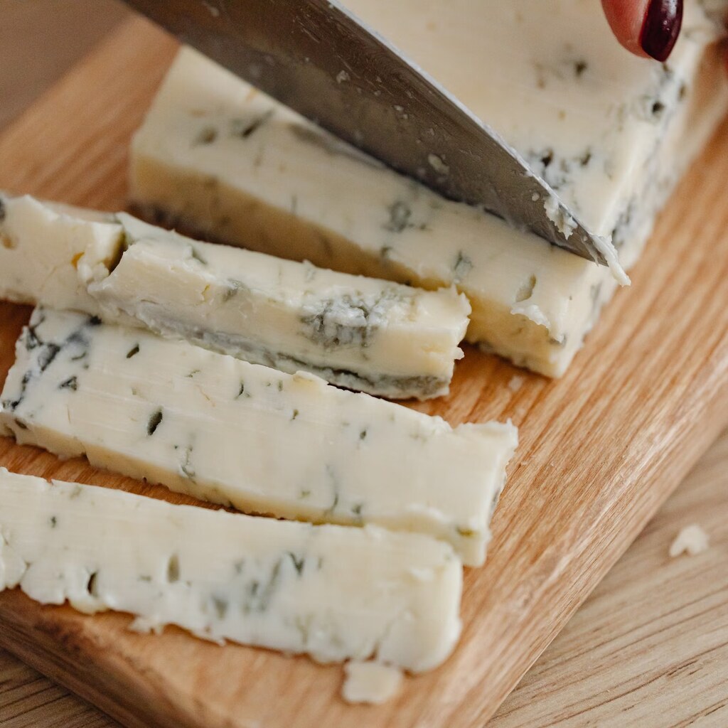 A photo of Gorgonzola cheese being sliced on a wooden board.