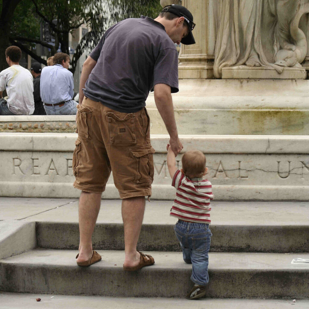 Photo of a man helping a toddler up some steps