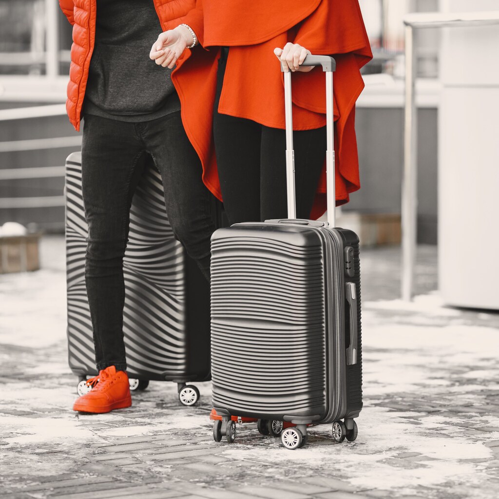 A photo of two rolling suitcases beside travelers outdoors