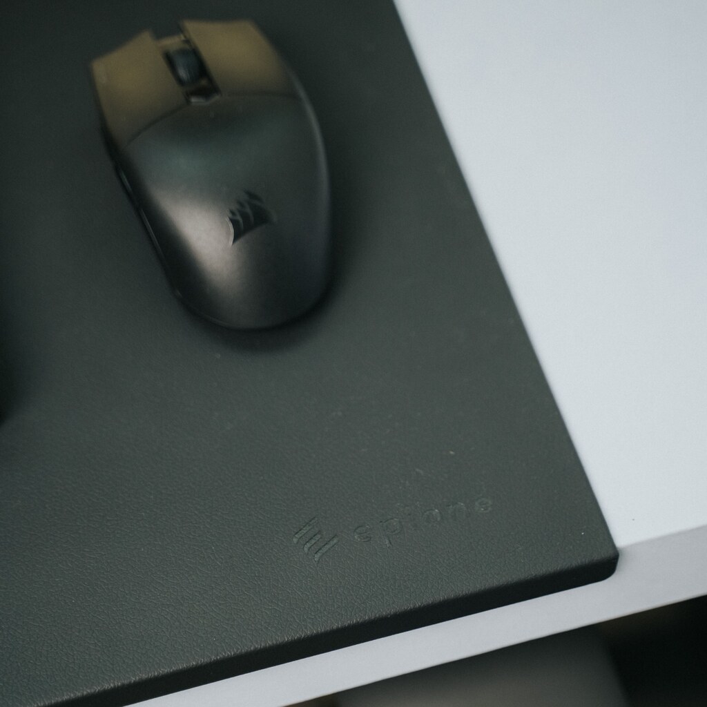 A photo of a black mouse pad with a computer mouse on a desk.