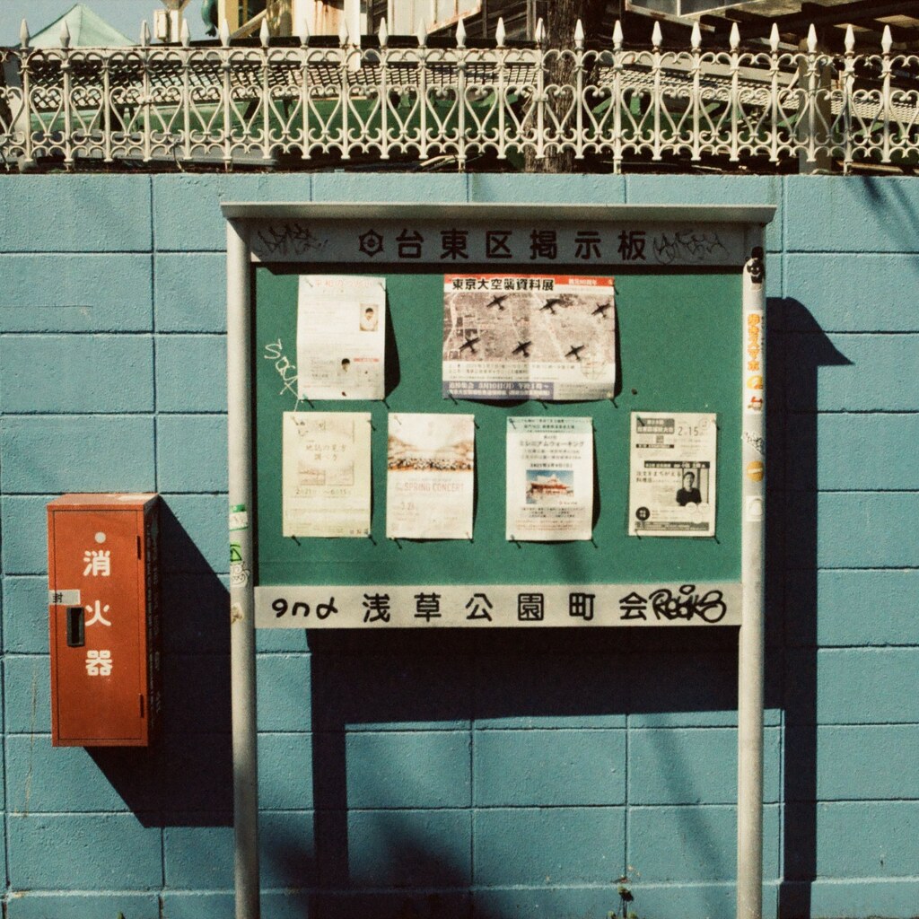 A photo of a vintage noticeboard with posted papers mounted on a blue brick wall