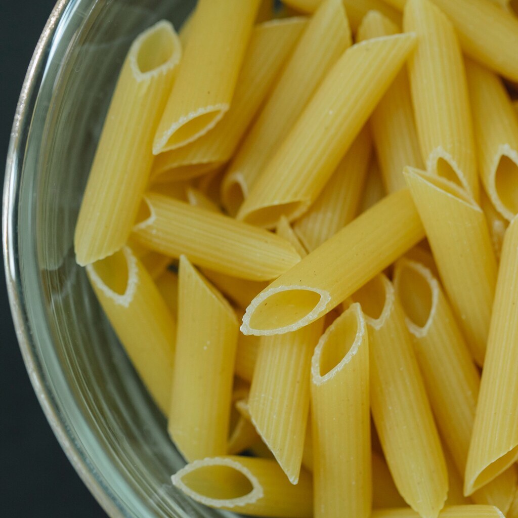 A photo of uncooked penne pasta in a glass bowl.