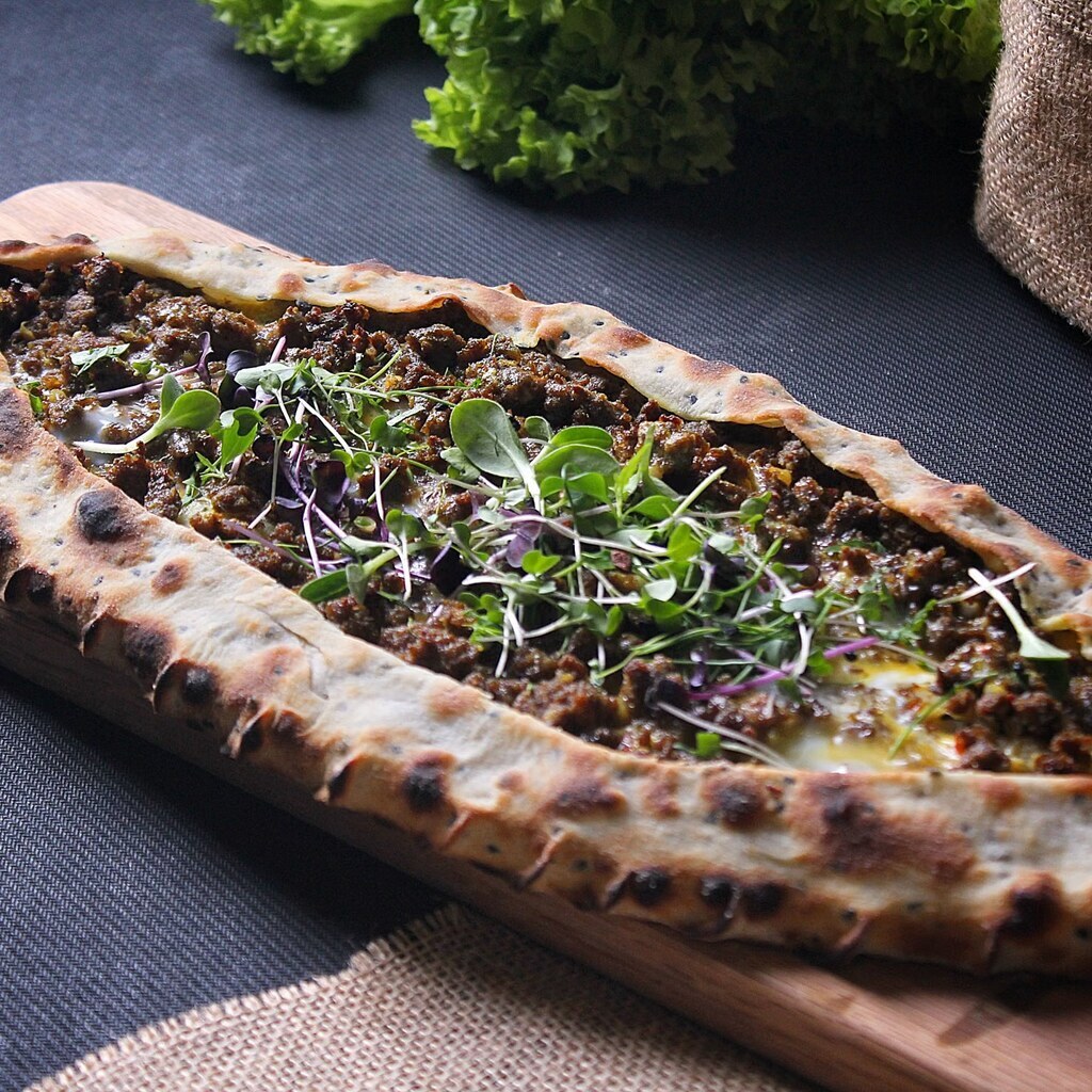 A photo of a boat-shaped Turkish pide topped with minced meat and greens.