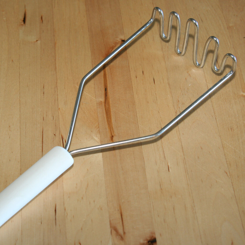 A photo of a wire potato masher with a white handle on a wooden surface