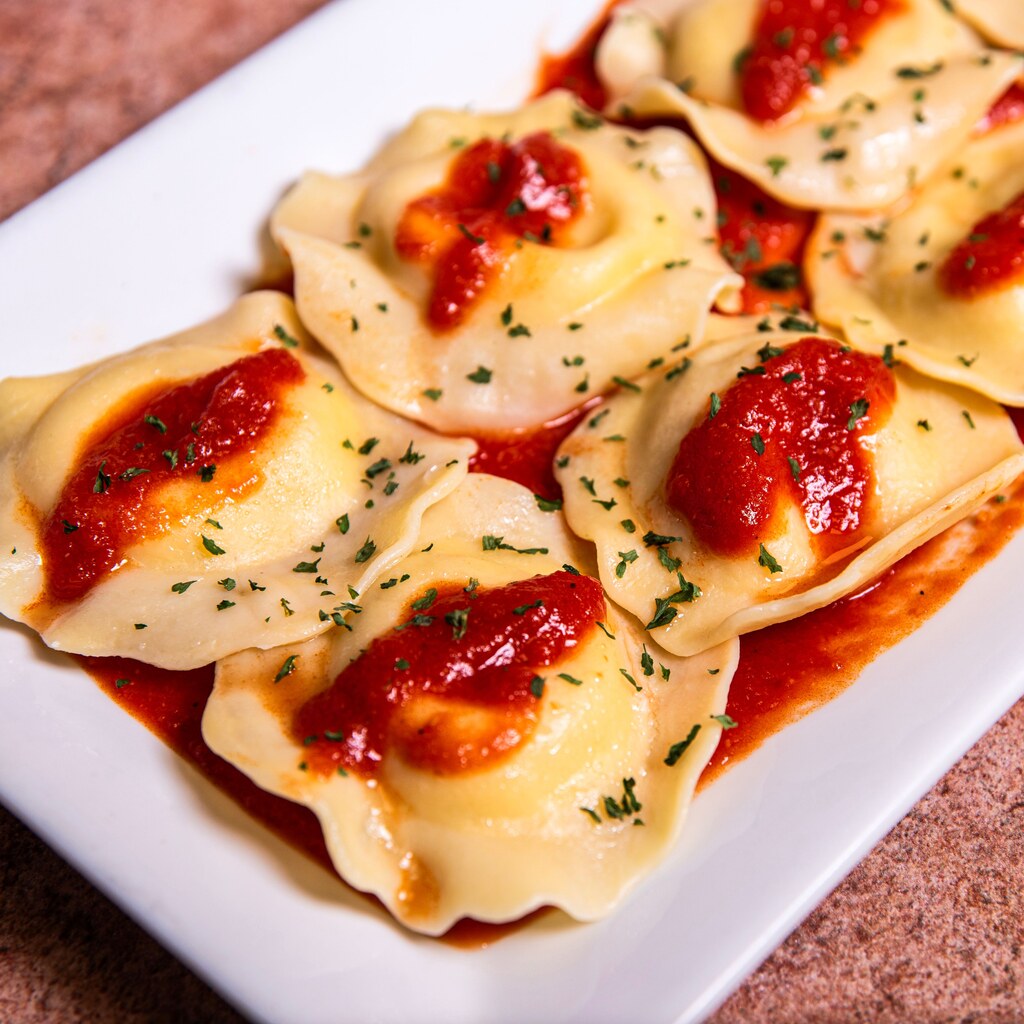 A photo of ravioli topped with tomato sauce and herbs on a white plate