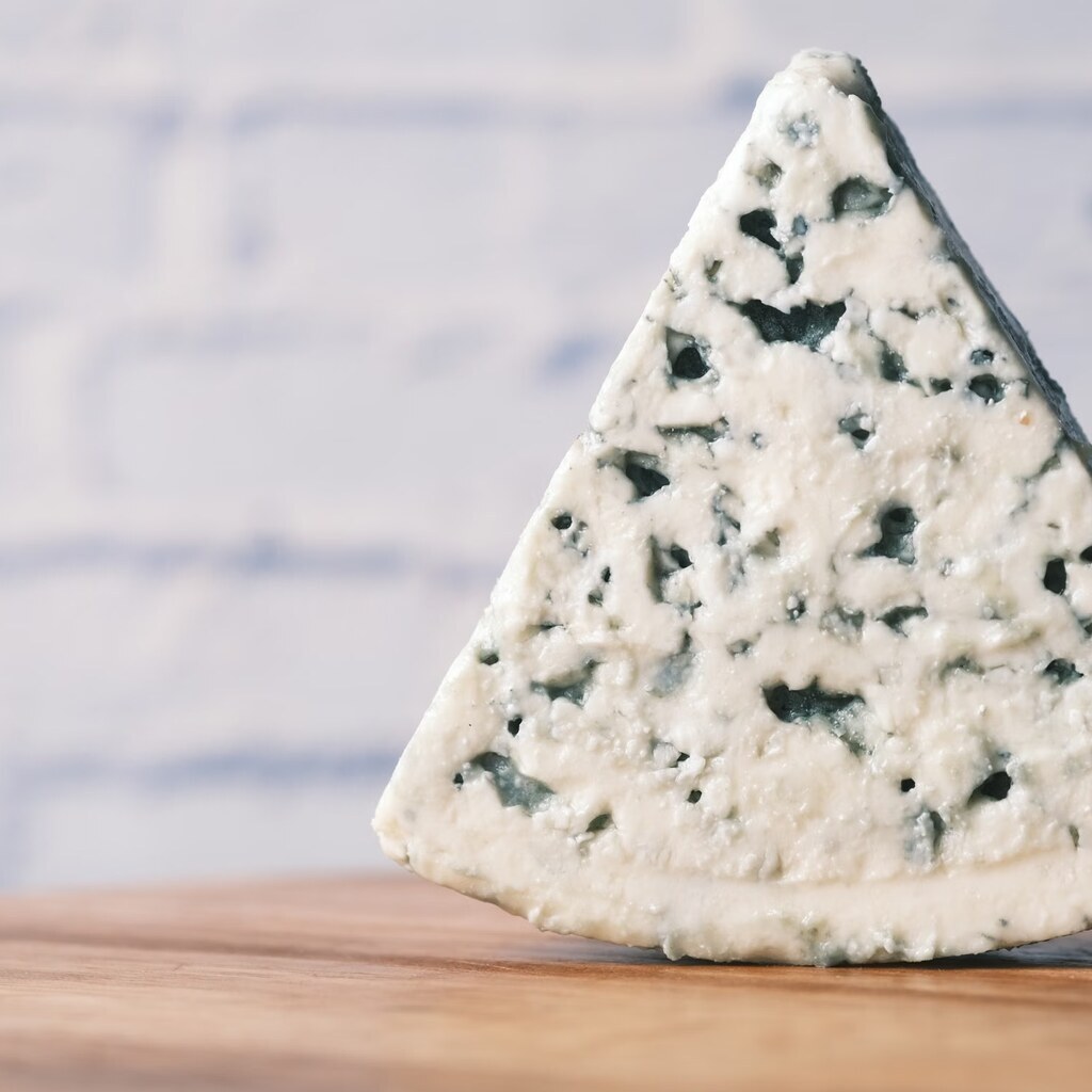 A photo of a wedge of Stilton cheese on a wooden surface.