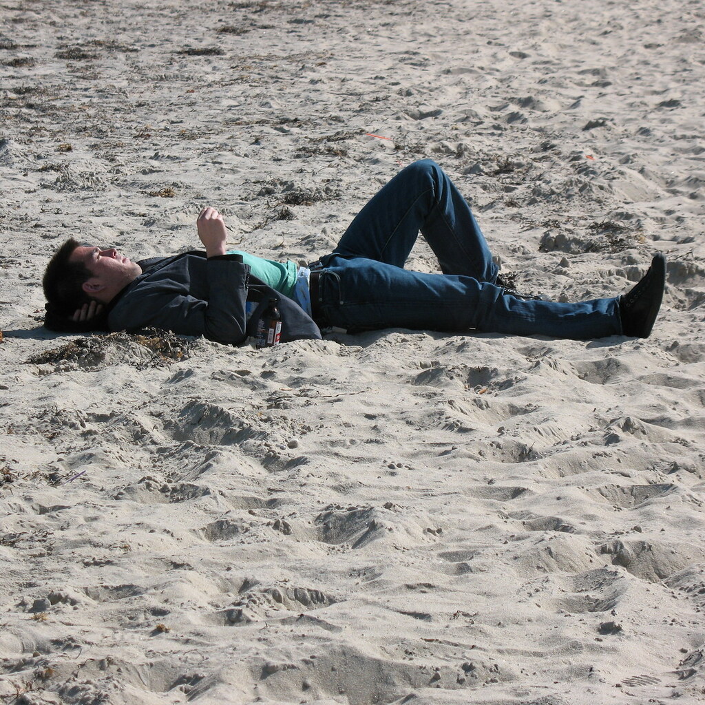 A man lying supine on a beach