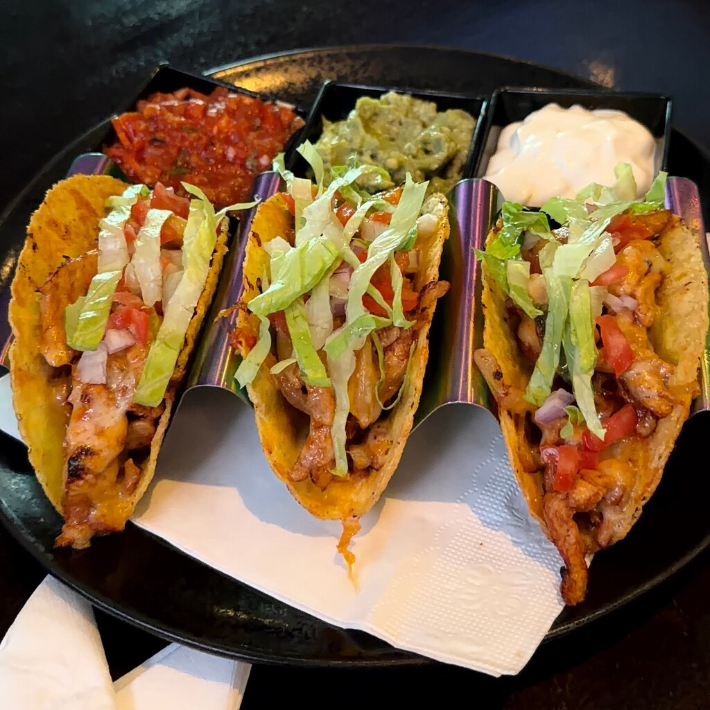 A photo of three crispy taco shells filled with meat, lettuce, tomatoes, and toppings on a black plate