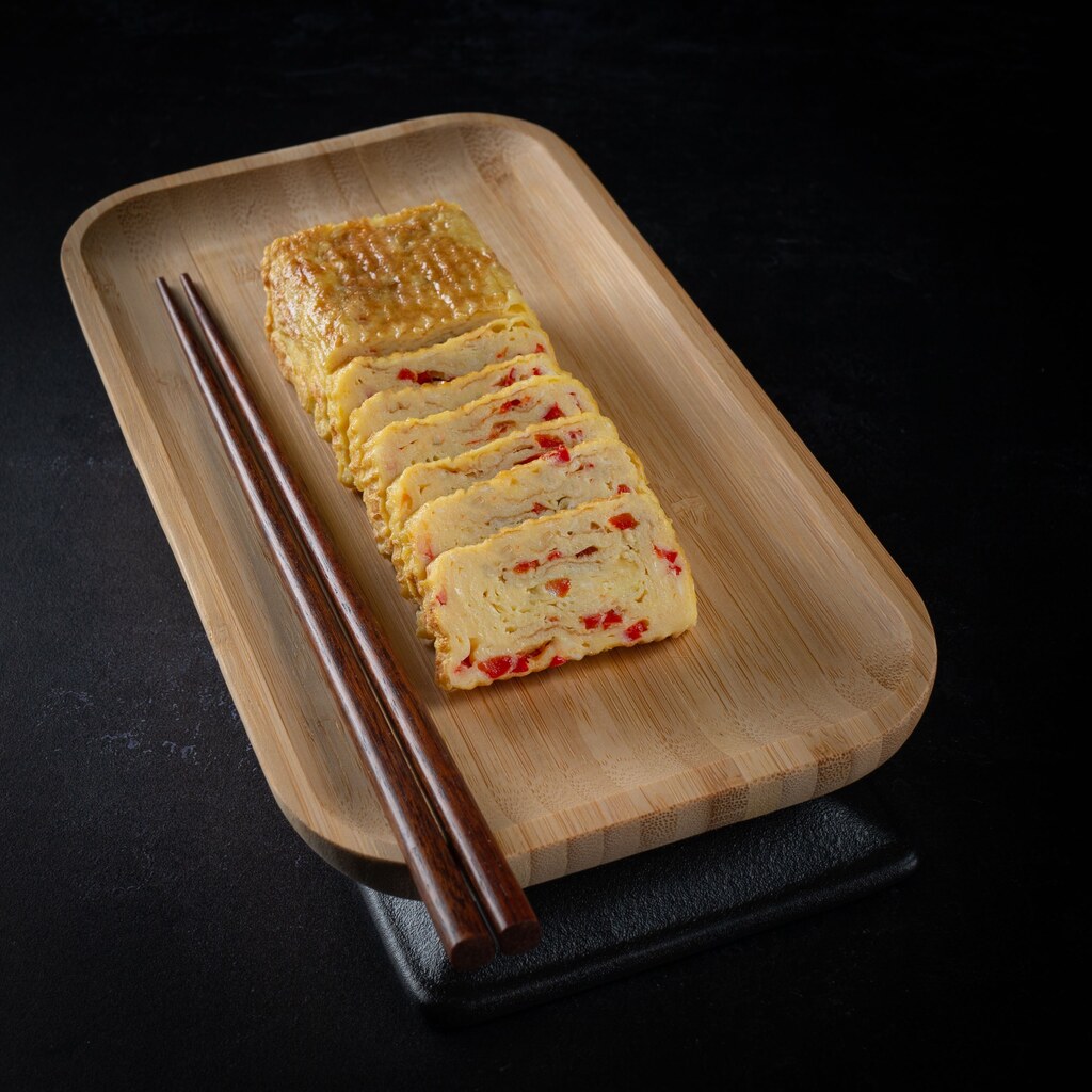 A photo of sliced tamagoyaki arranged on a bamboo tray with chopsticks