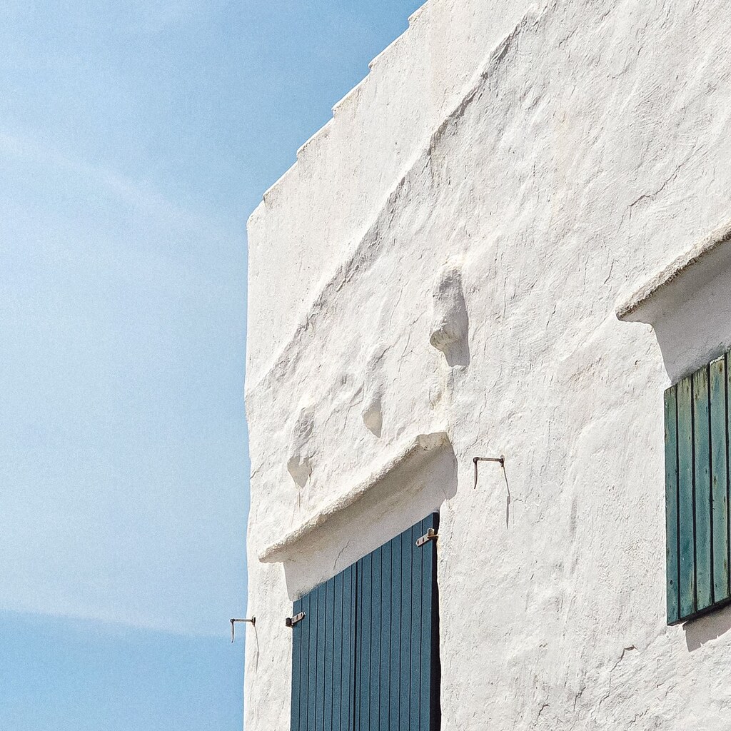 A photo of a whitewashed building with blue shutters under a blue sky.